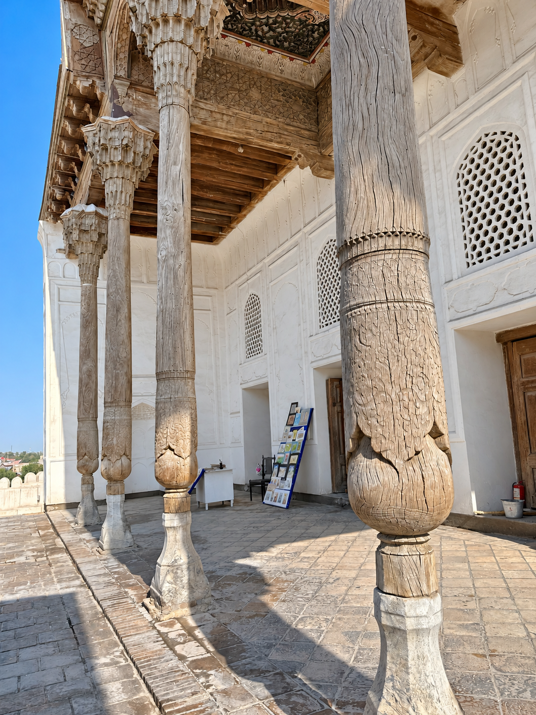 Sunlight illuminating weathered carved wooden columns during a visit to the Ark of Bukhara