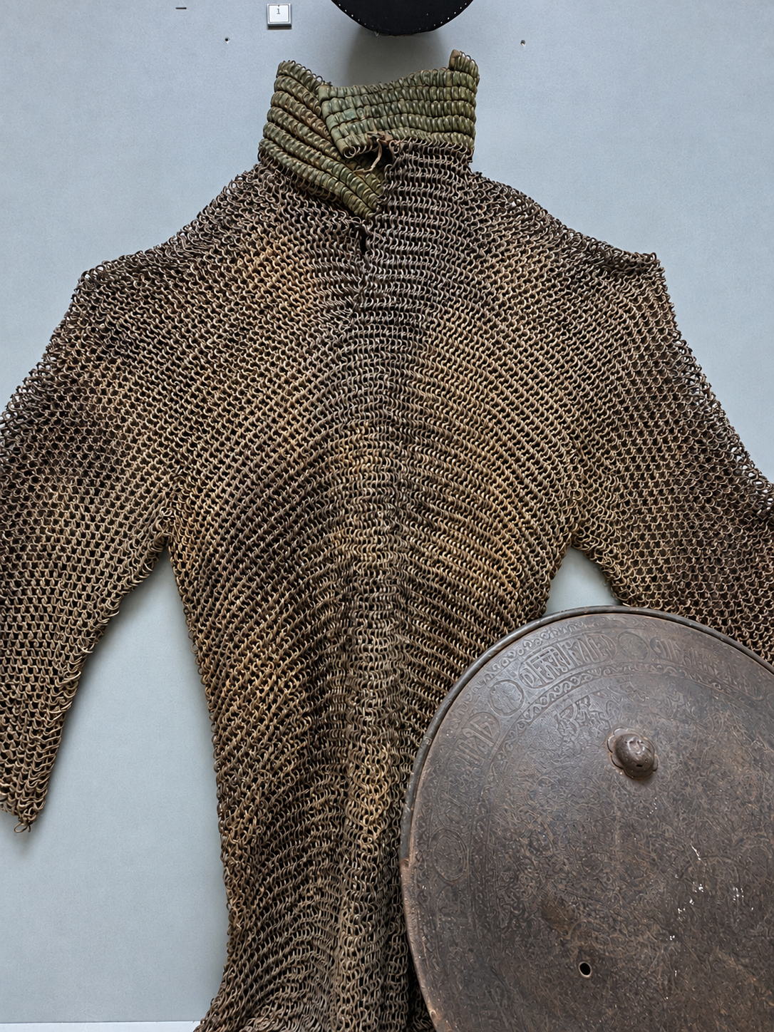 Chain-mail armor and a decorated round shield on display in the Ark of Bukhara museum