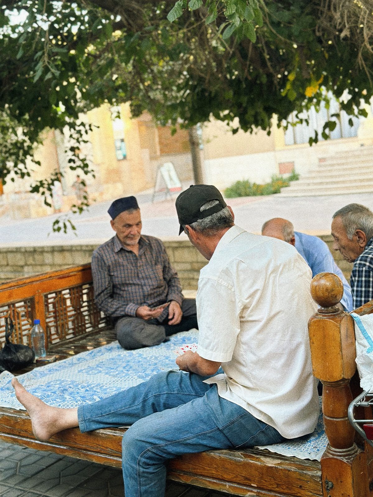 Men sitting together on a raised wooden platform in the shade in Bukhara