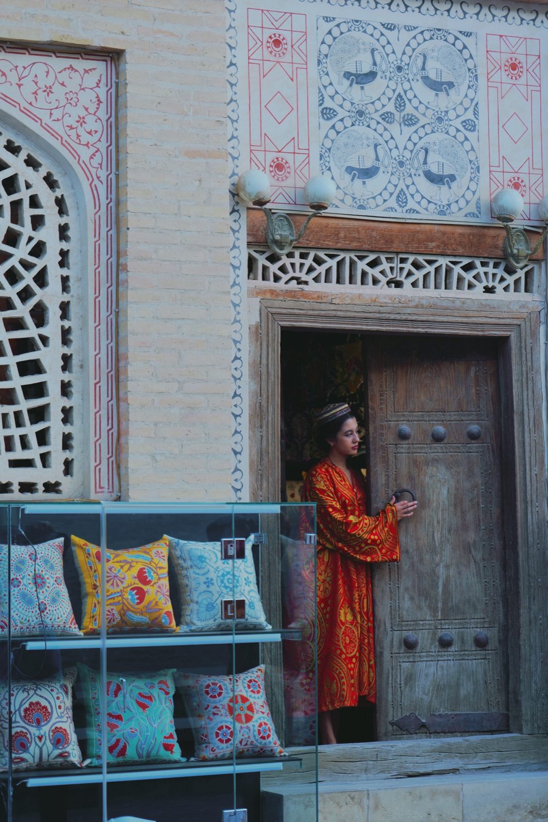 A woman in a red patterned dress at a Bukhara shop with embroidered cushions